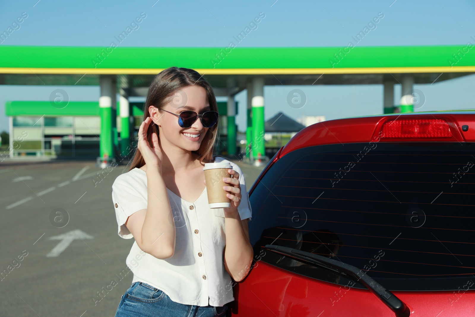 Photo of Beautiful young woman with coffee near car at gas station