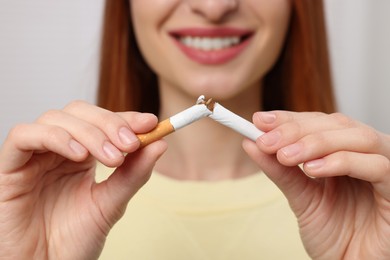 Stop smoking concept. Woman breaking cigarette on light gray background, closeup