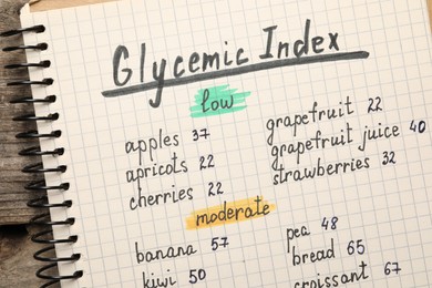 Photo of List with products of low and moderate glycemic index in notebook on wooden table, top view