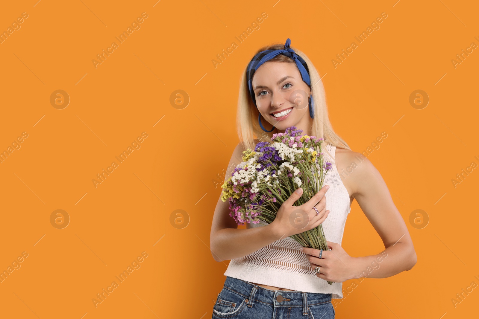 Photo of Happy hippie woman with bouquet of flowers on orange background. Space for text