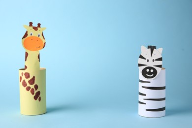 Photo of Toy giraffe and zebra made from toilet paper hubs on light blue background, space for text. Children's handmade ideas