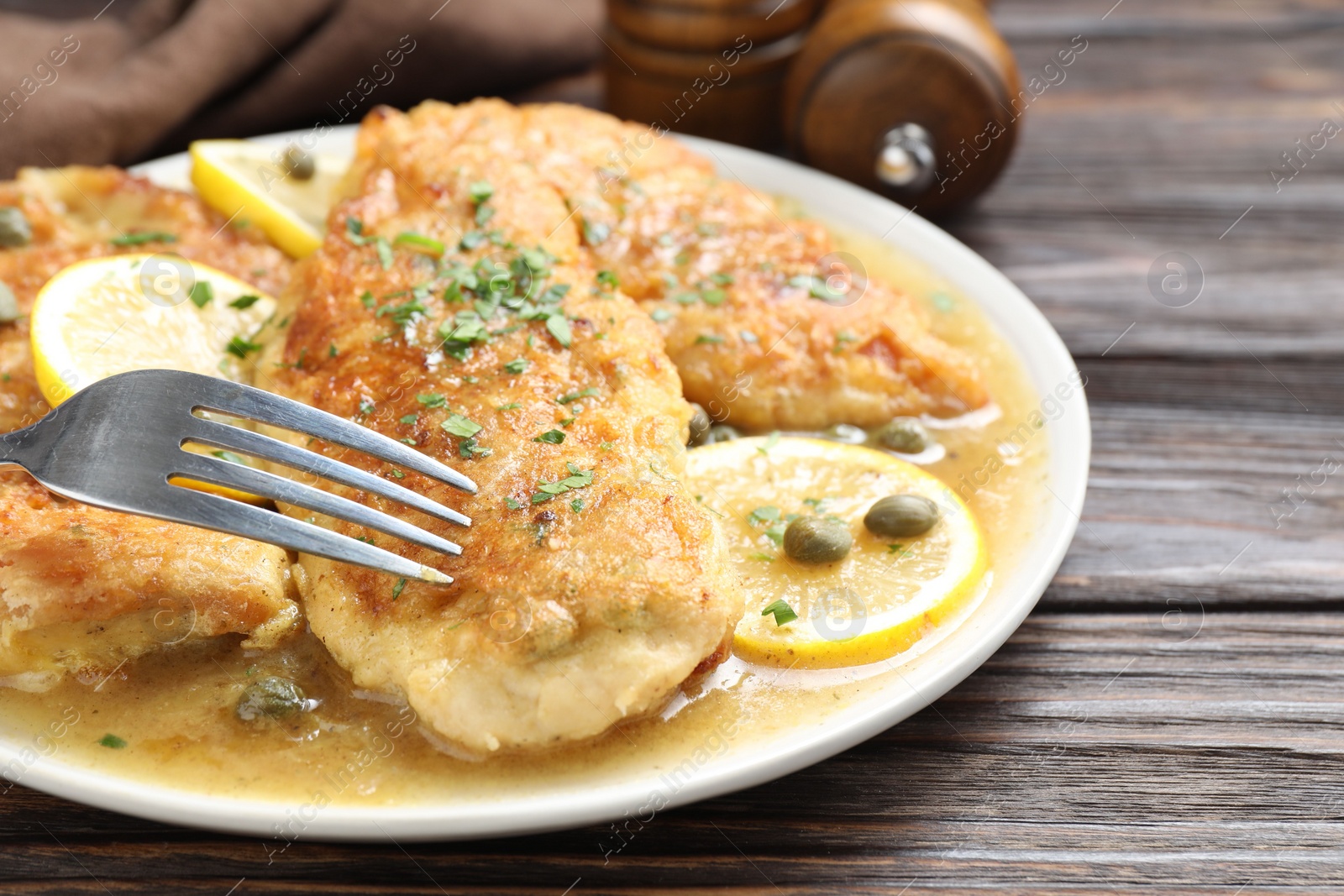 Photo of Delicious chicken piccata on wooden table, closeup