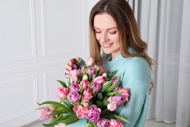 Photo of Happy young woman with bouquet of beautiful tulips indoors