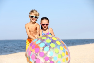 Photo of Little children with inflatable ball on sandy beach near sea. Summer holidays