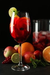 Photo of Glass and jug of Red Sangria with fruits on black table
