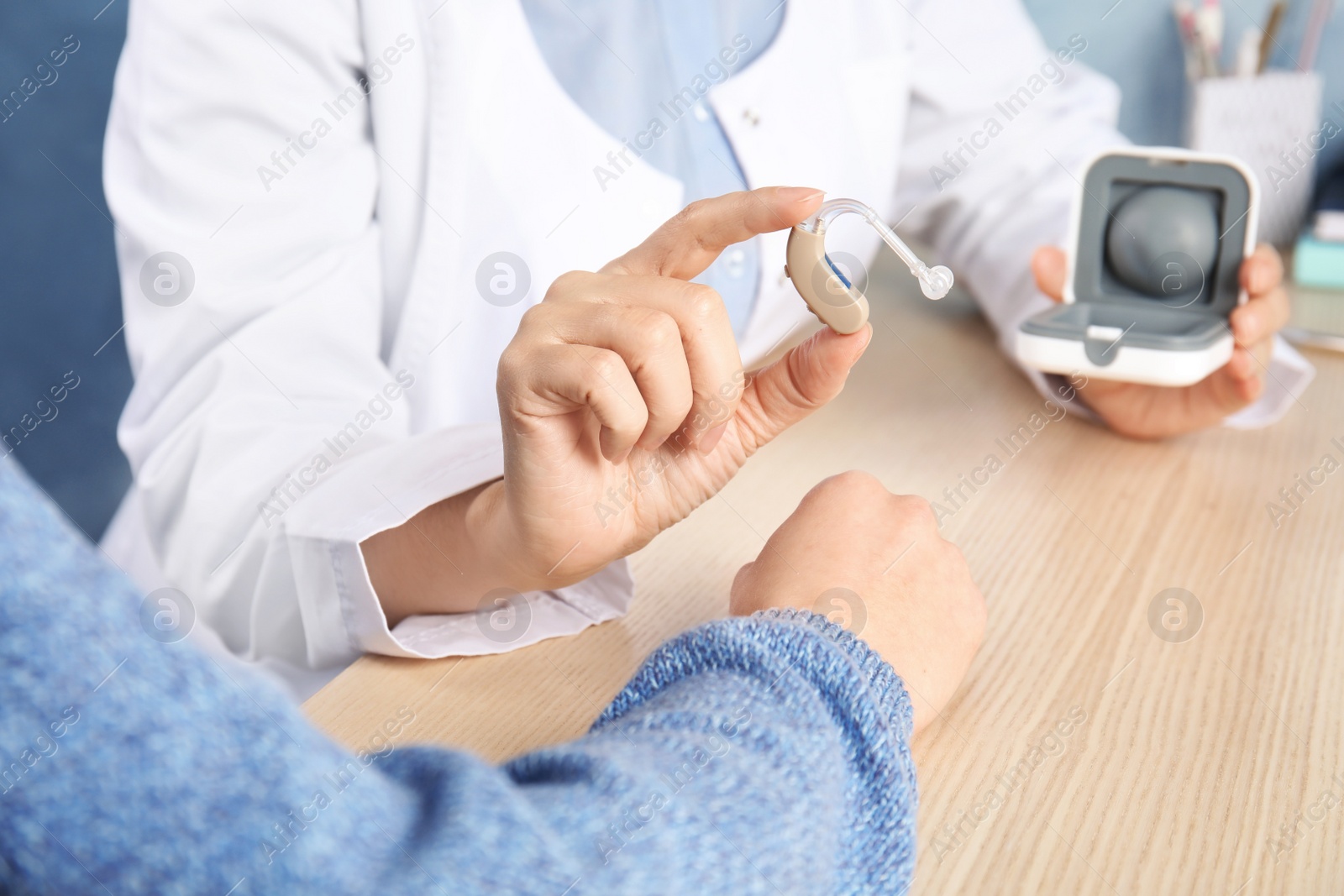 Photo of Doctor giving patient hearing aid at table in clinic, closeup