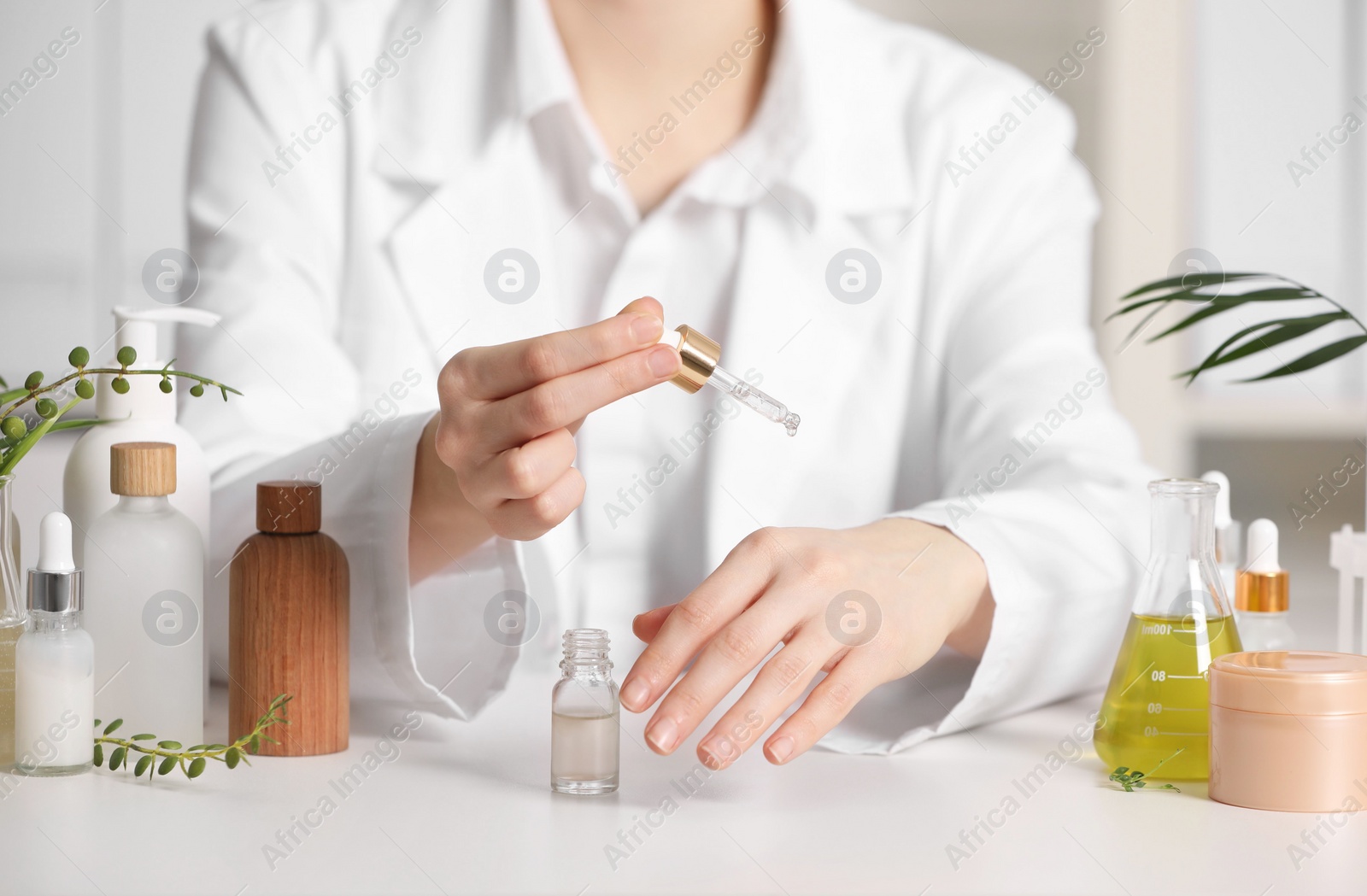 Photo of Dermatologist testing essential oil at white table indoors, closeup