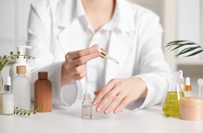 Photo of Dermatologist testing essential oil at white table indoors, closeup