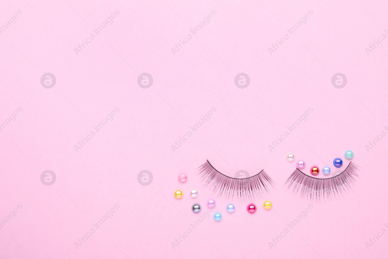 Photo of False eyelashes and colorful beads on pink background, flat lay. Space for text