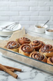 Baking dish with tasty cinnamon rolls and sticks on white marble table