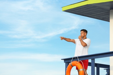 Photo of Male lifeguard with whistle on watch tower against blue sky