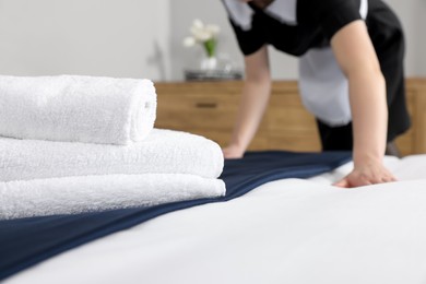 Photo of Maid making bed in hotel room, closeup. Focus on towels