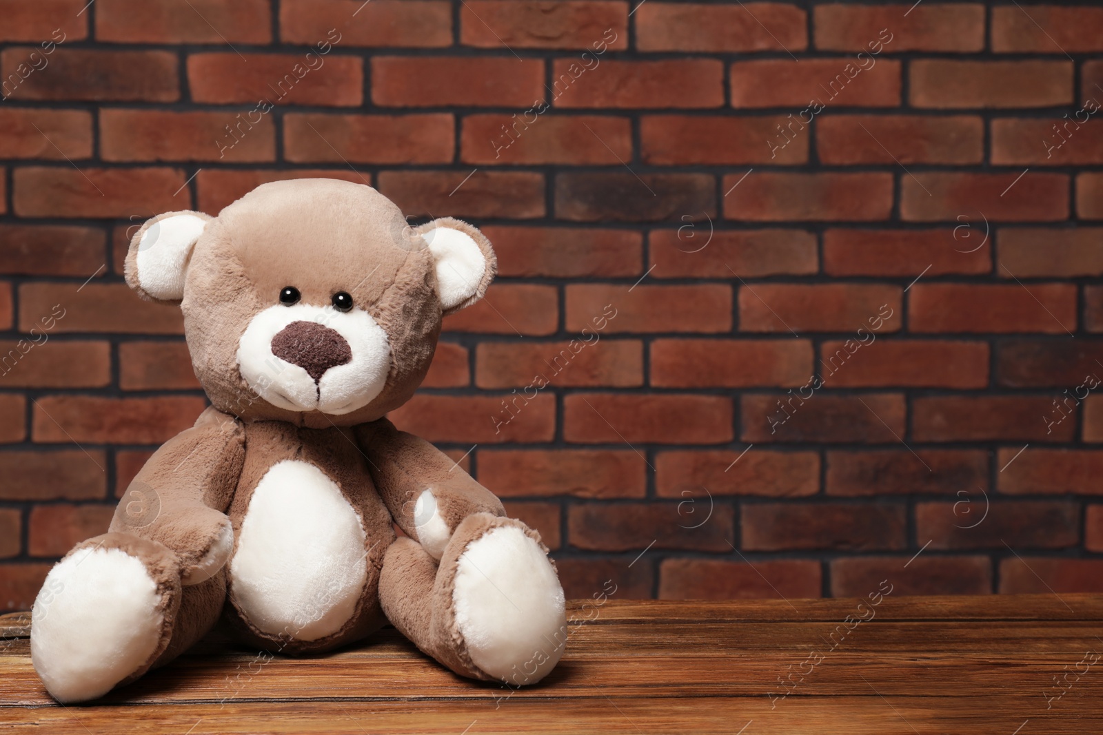 Photo of Cute teddy bear on wooden table near brick wall, space for text