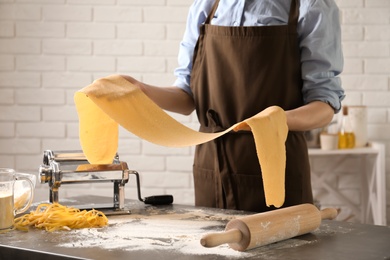 Young woman preparing dough for pasta at table