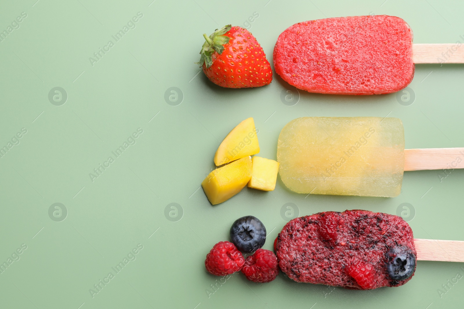 Photo of Different fruit ice pops on pale green background, flat lay. Space for text