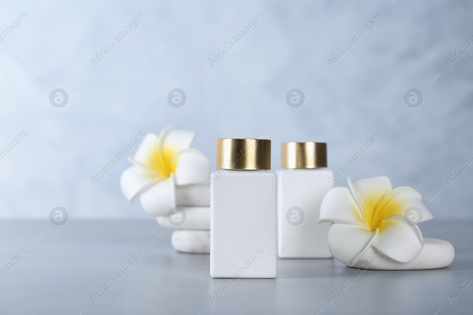 Photo of Cosmetic products, spa stones and tropical flowers on light grey table