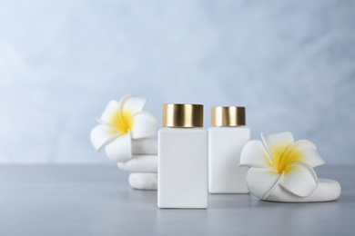 Photo of Cosmetic products, spa stones and tropical flowers on light grey table