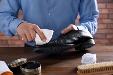 Man cleaning leather shoe at wooden table indoors, closeup