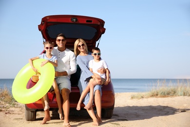 Photo of Happy family with inflatable ring near car at beach on sunny day