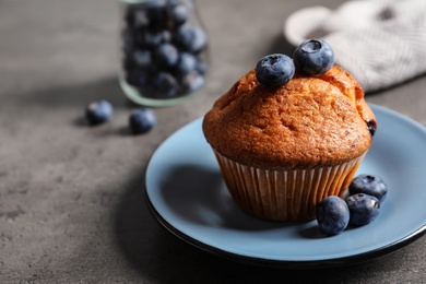 Photo of Plate with tasty muffin and blueberries on grey table
