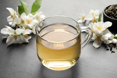 Photo of Glass cup of jasmine tea and fresh flowers on dark grey table