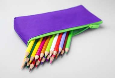 Many colorful pencils in pencil case on light grey background, closeup