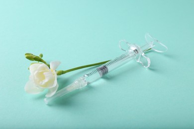 Photo of Cosmetology. Medical syringe and freesia flower on turquoise background, closeup