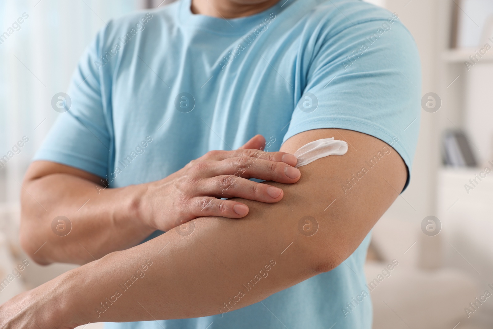 Photo of Man applying body cream onto his arm indoors, closeup