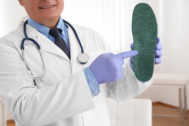 Photo of Senior male orthopedist showing insole in clinic, closeup