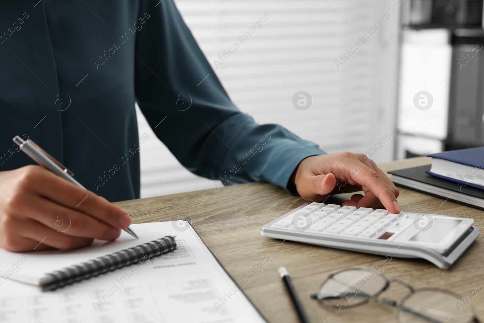 Photo of Woman using calculator while taking notes at wooden table, closeup