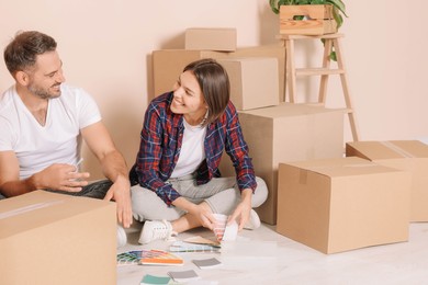 Photo of Happy couple surrounded by moving boxes choosing colors in new apartment
