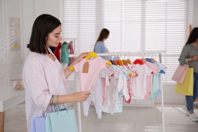 Photo of Happy pregnant woman with shopping bags choosing baby clothes in store