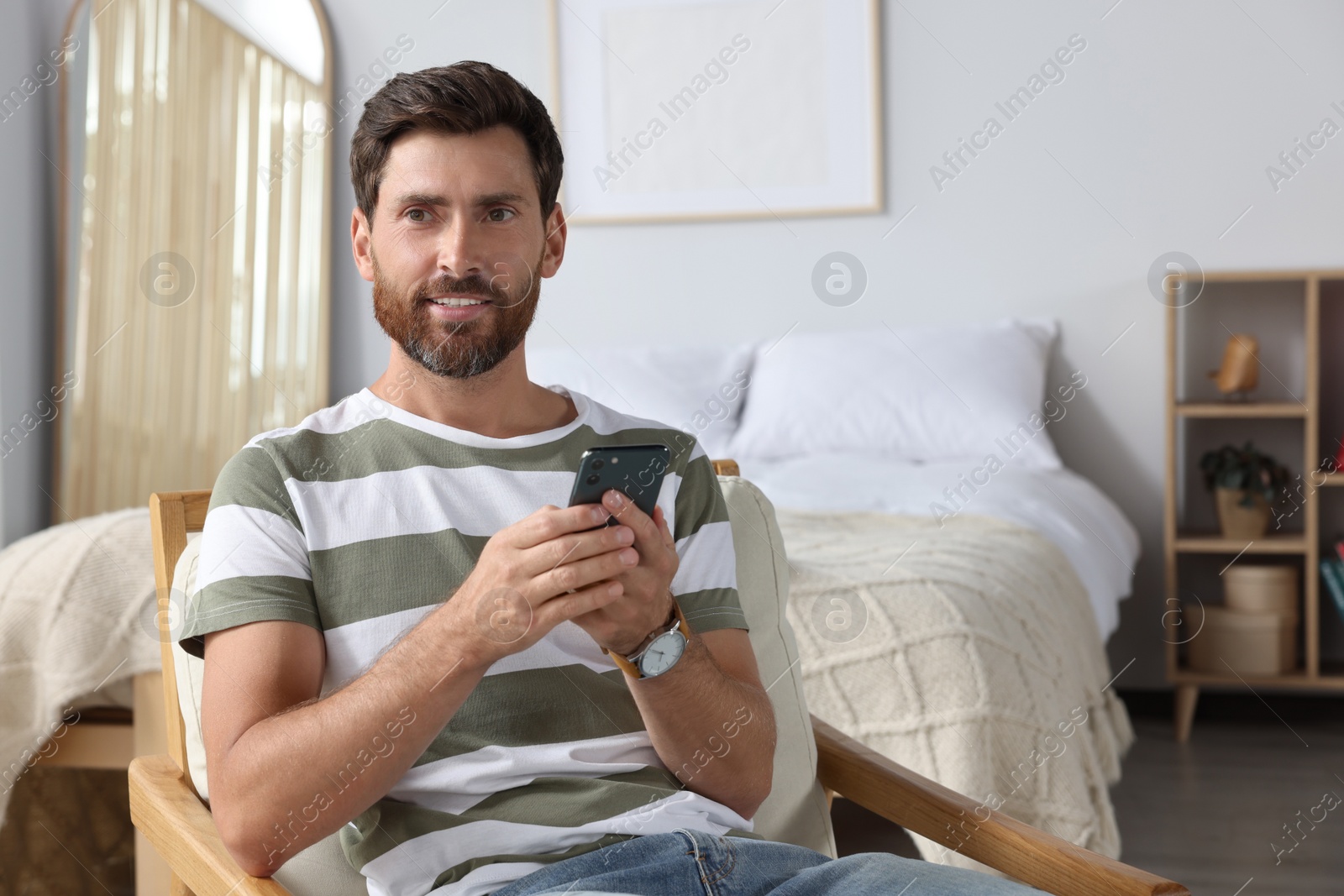 Photo of Handsome man using smartphone in bedroom, space for text