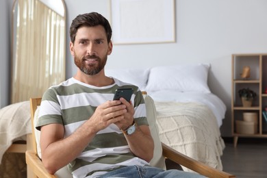 Handsome man using smartphone in bedroom, space for text