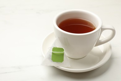 Tea bag and cup of hot beverage on white table, space for text