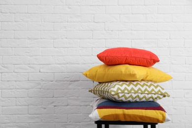 Photo of Many different pillows on chair near brick wall with space for text