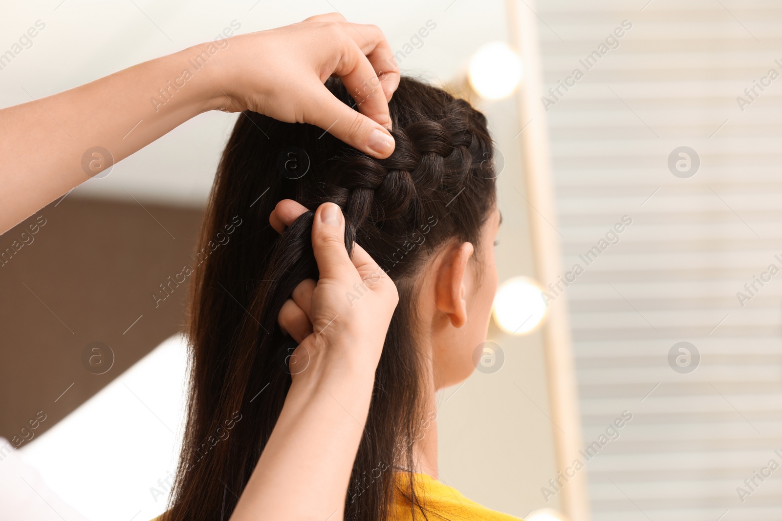 Photo of Professional stylist braiding client's hair in salon