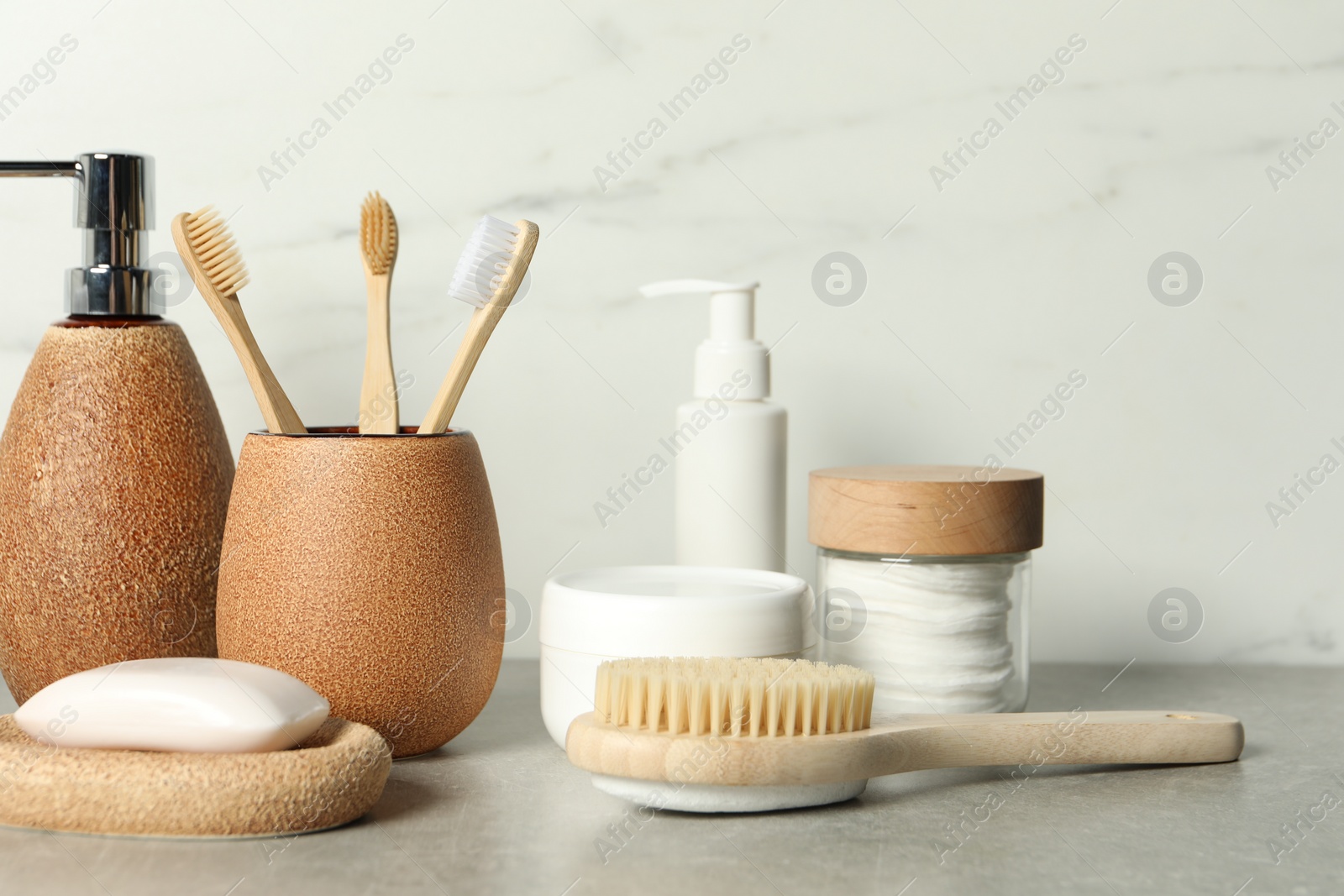 Photo of Different bath accessories and personal care products on gray table near white marble wall