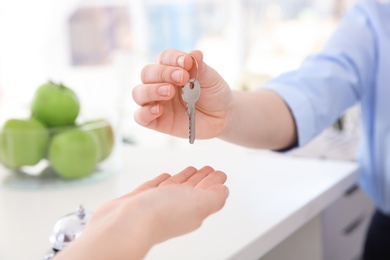 Female receptionist giving key to young woman in hotel, closeup