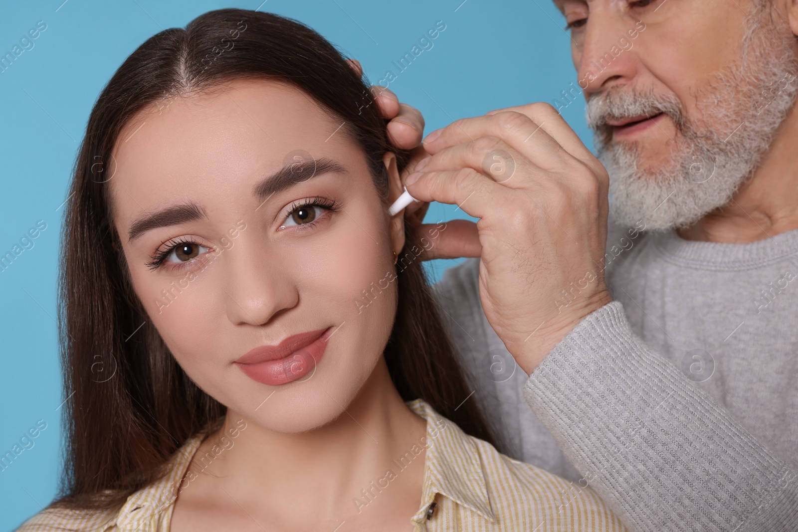 Photo of Senior man dripping medication into woman's ear on light blue background, closeup