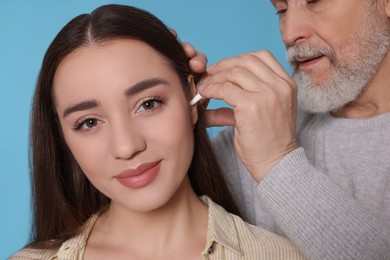 Senior man dripping medication into woman's ear on light blue background, closeup