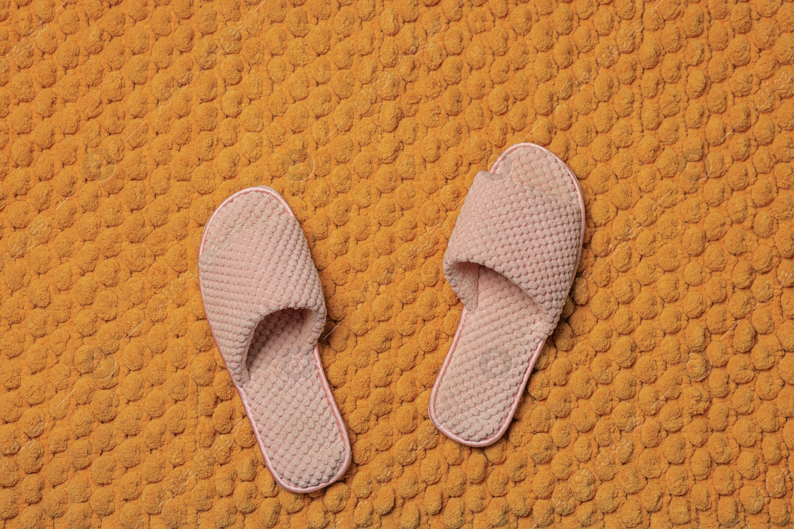 Photo of Slippers on soft orange bath mat, flat lay