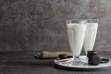 Glasses of milk with chocolate cookies on table against grey background, space for text