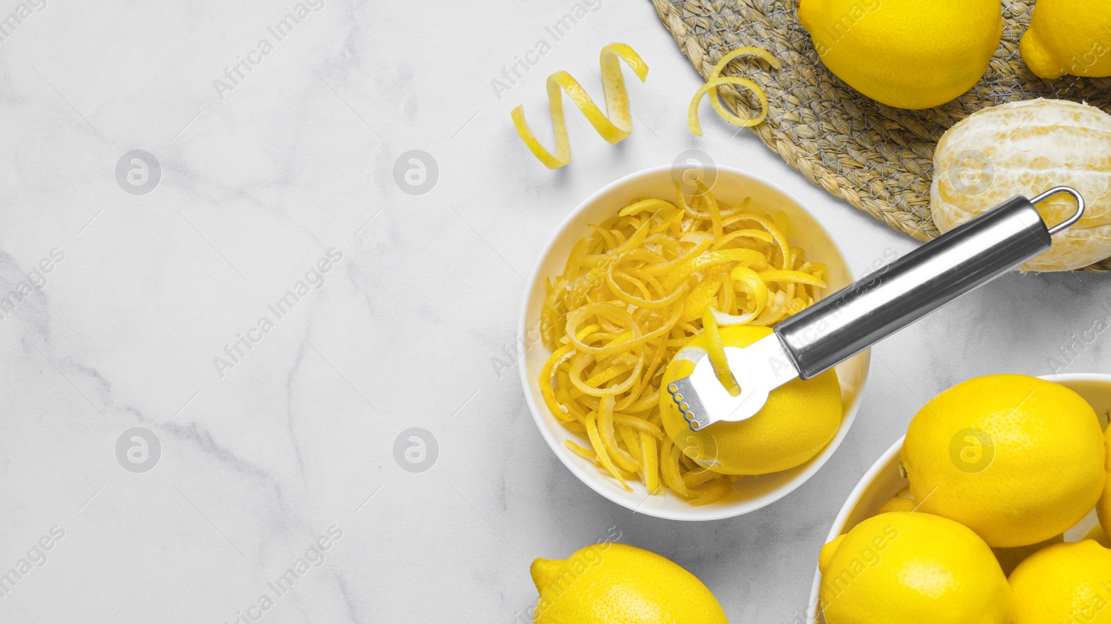 Photo of Bowl with peel pieces, fresh lemons and zester on white marble table, flat lay. Space for text