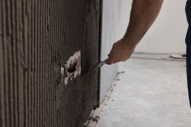 Photo of Worker spreading adhesive mix on wall for tile installation indoors, closeup