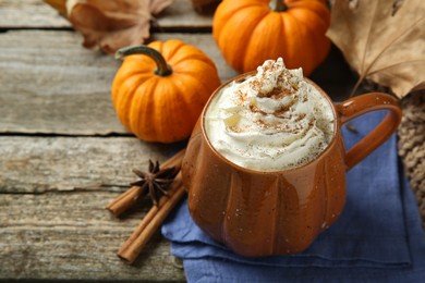 Photo of Mug of pumpkin spice latte with whipped cream and ingredients on wooden table, closeup. Space for text