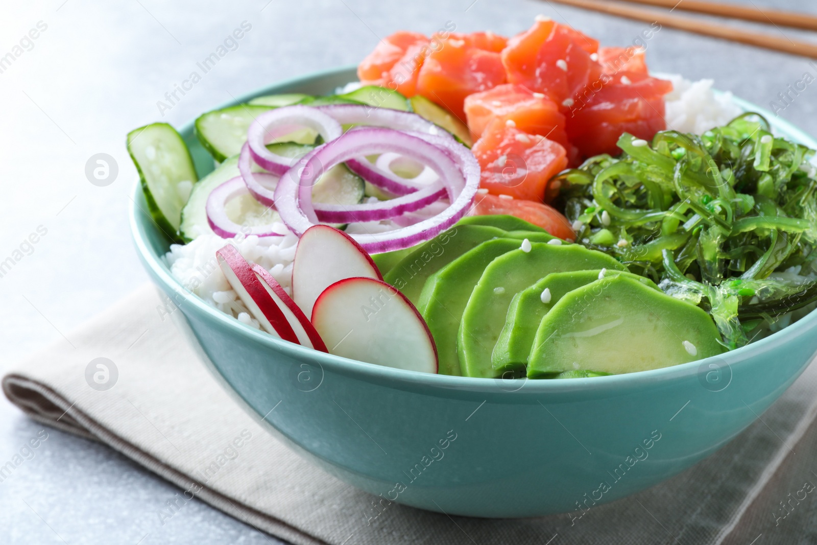 Photo of Delicious poke bowl with salmon, seaweed and vegetables served on light grey table, closeup