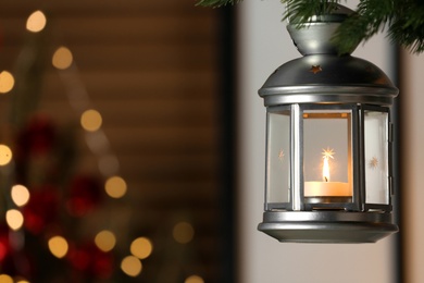 Photo of Beautiful Christmas lantern with burning candle hanging on fir tree branch in room. Space for text