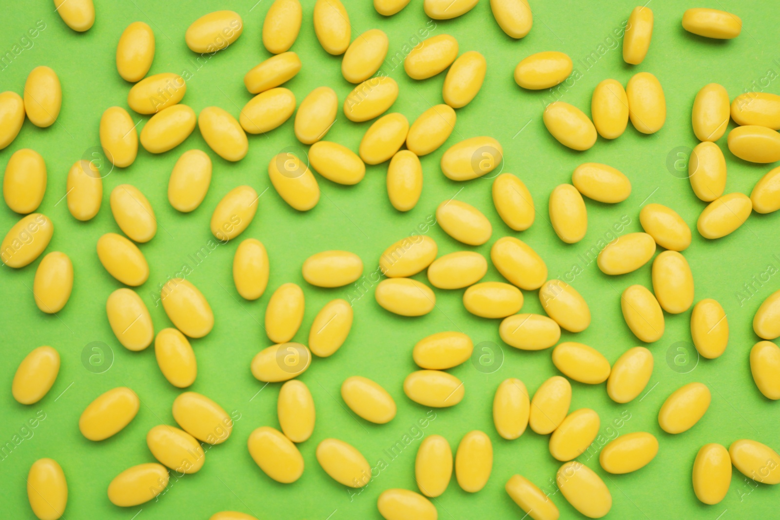 Photo of Many yellow dragee candies on green background, flat lay