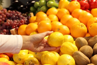 Photo of Woman picking fresh lemon at market, closeup